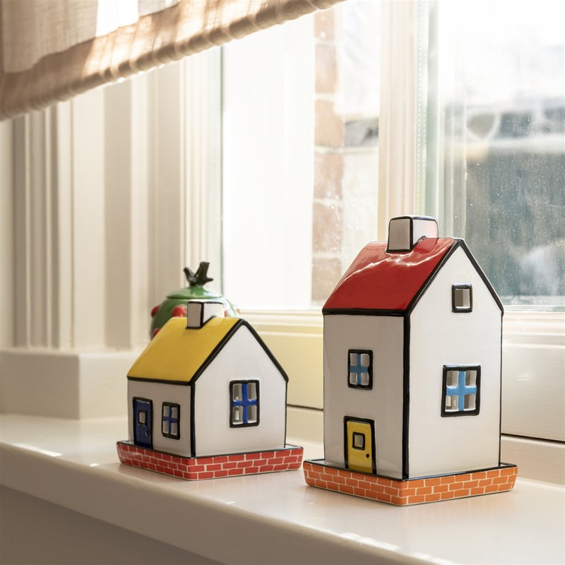 Two small house-shaped decorative tealight holders on a windowsill with a blurred window background.