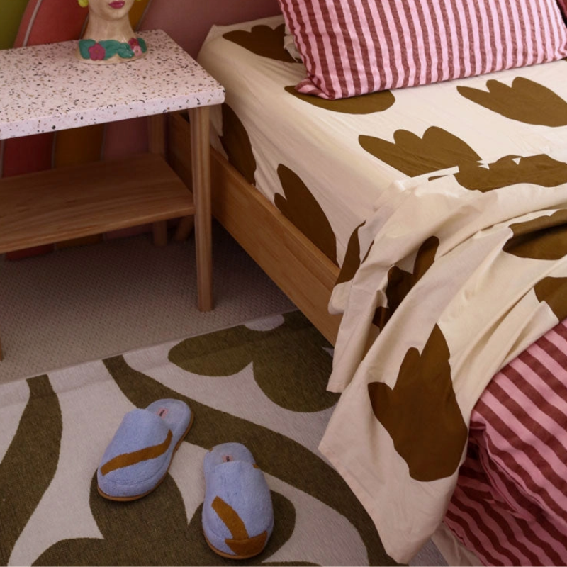 Children's bedroom with floral-patterned bedspread, striped pillows, and slippers on a rug.