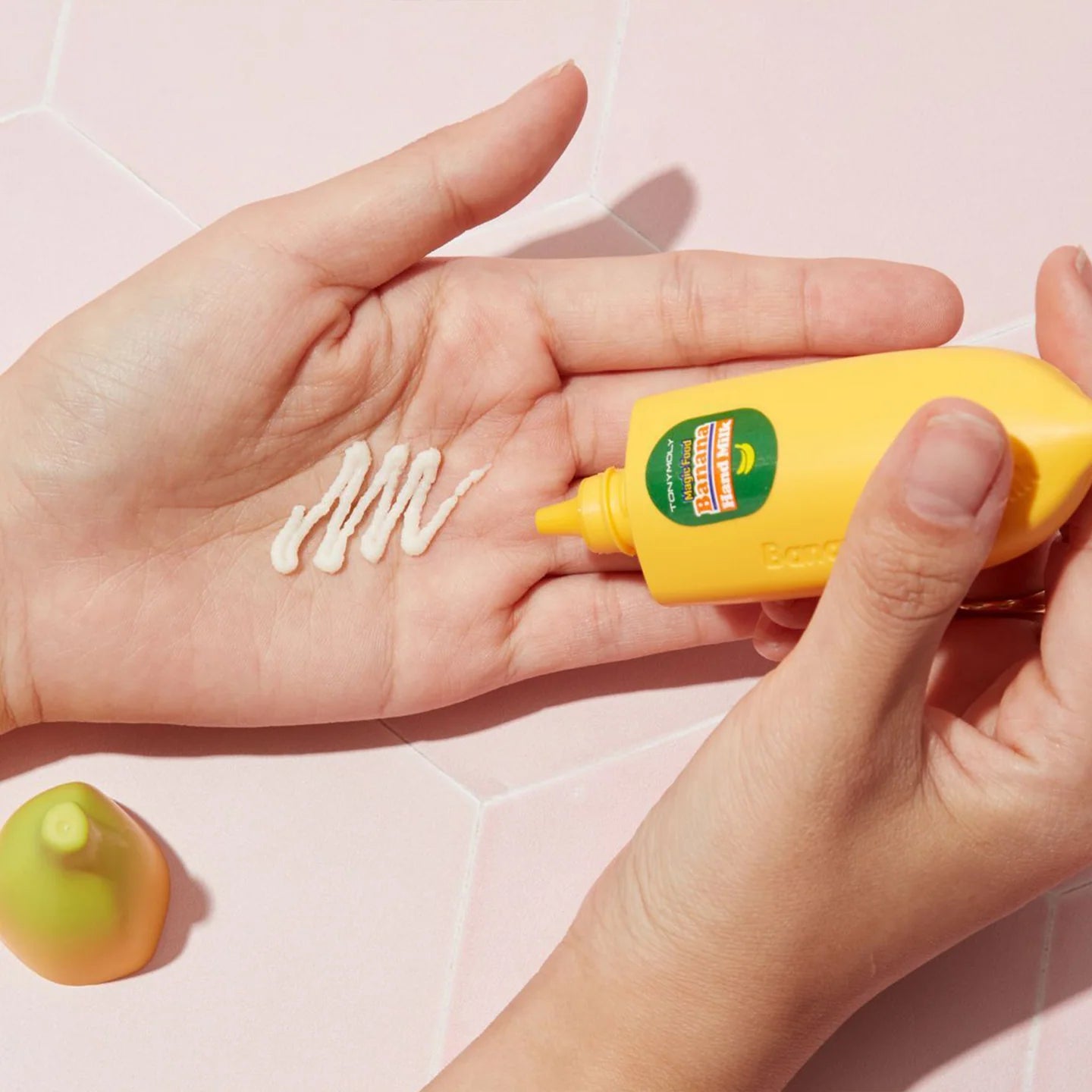 Hand holding a yellow bottle of sunscreen with a small amount on the palm against a light pink background
